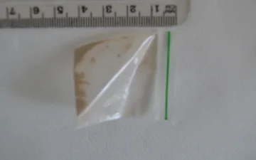 Kleines Tütchen mit braunen Heroinresten neben einem Lineal